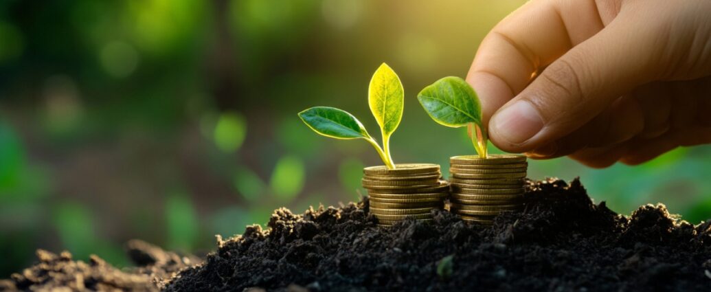 Close-up of a hand placing a small plant on a stack of coins growing from rich soil, symbolizing financial growth.