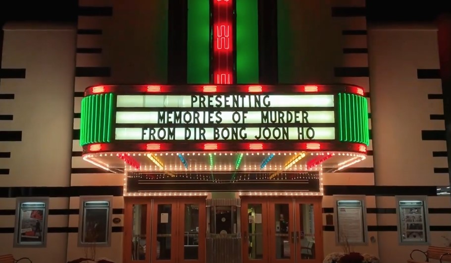 Neon lights paint the facade of a classic theater, showcasing the film "Memories of Murder