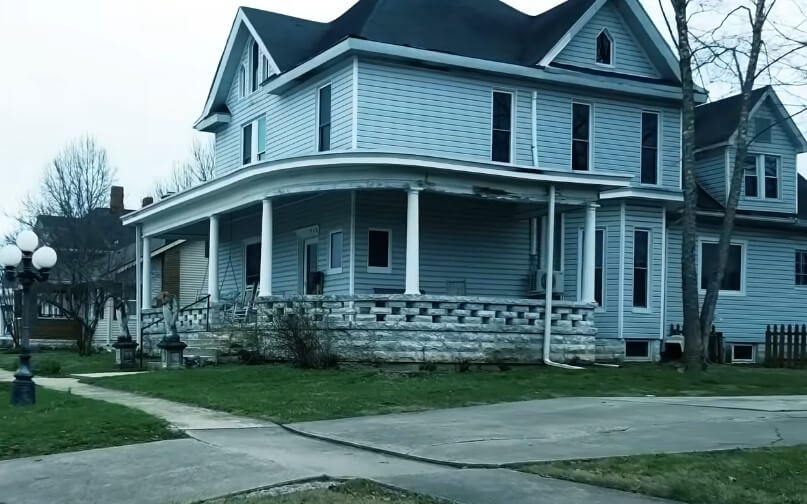 A light gray, historic home with a wide porch, nestled on a quiet street