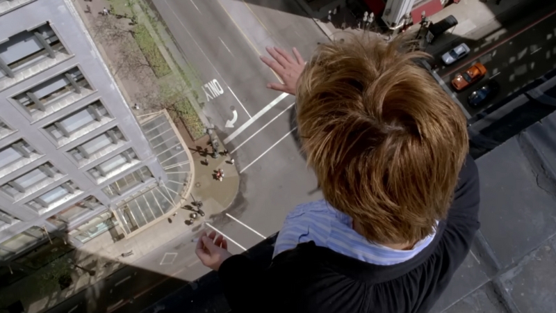 A man stands on the edge of a rooftop, looking down at a busy street in a tense scene from Stranger Than Fiction (2006)