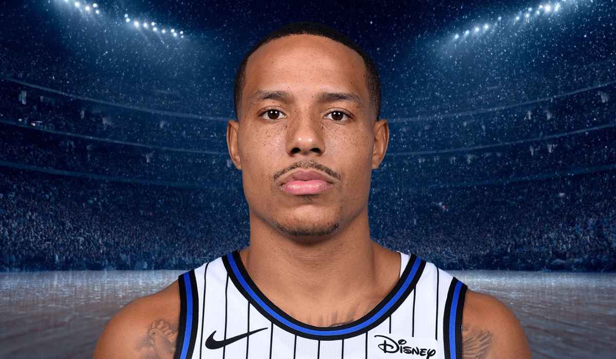 Basketball player wearing a white and blue striped jersey standing on the court under bright arena lights