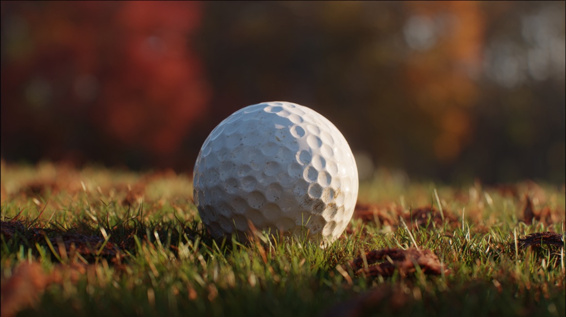 Close-up of a golf ball resting on grass with autumn foliage blurred in the background