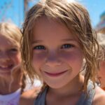 Three smiling children at an outdoor fair with colorful booths and rides in the background