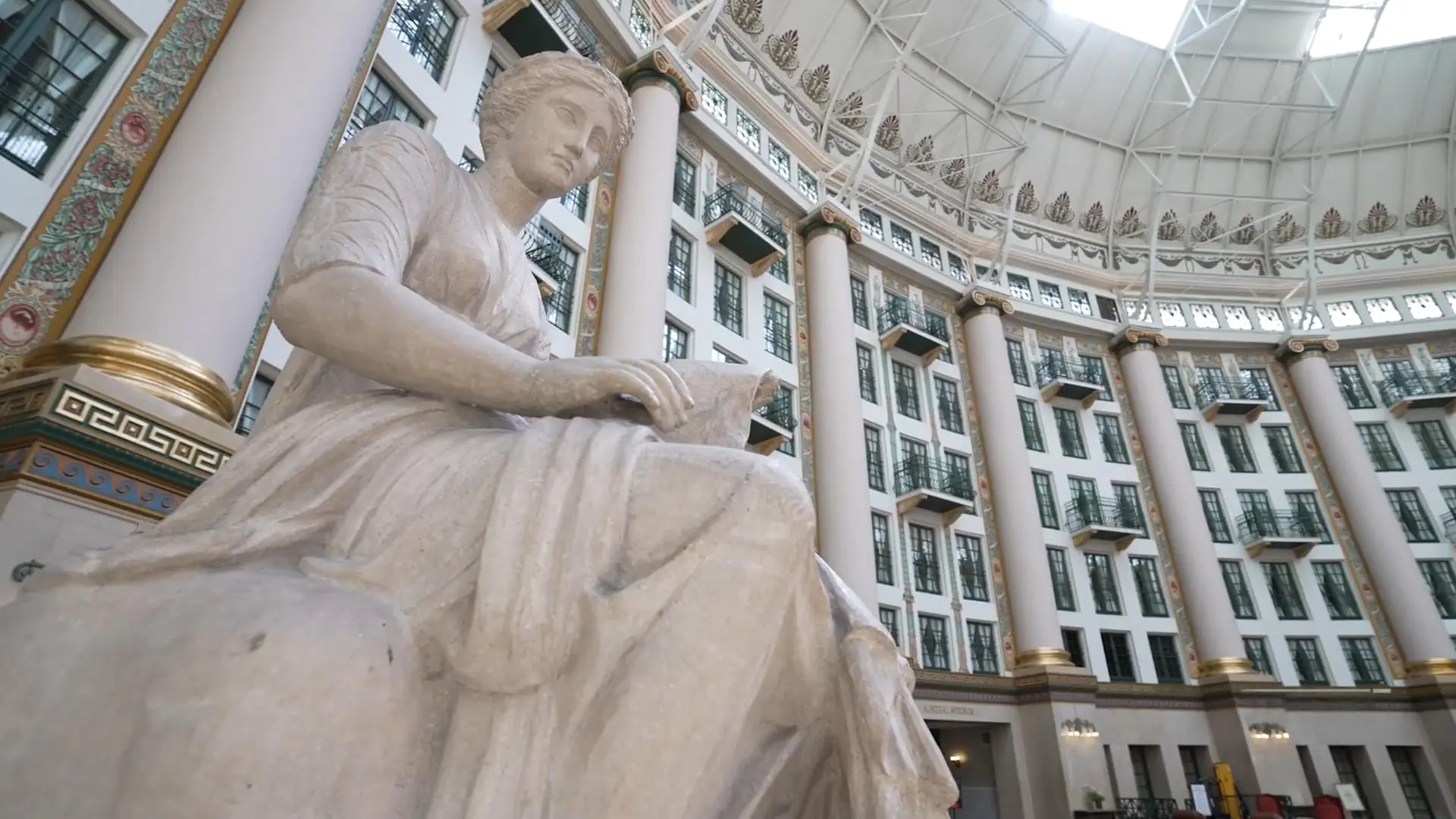 Large classical statue inside the grand atrium of a historic resort building with columns, balconies, and a domed ceiling