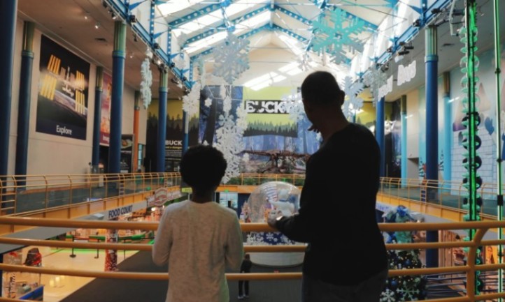 A silhouette of a child and adult look over a shopping mall balcony adorned with large snowflake decorations