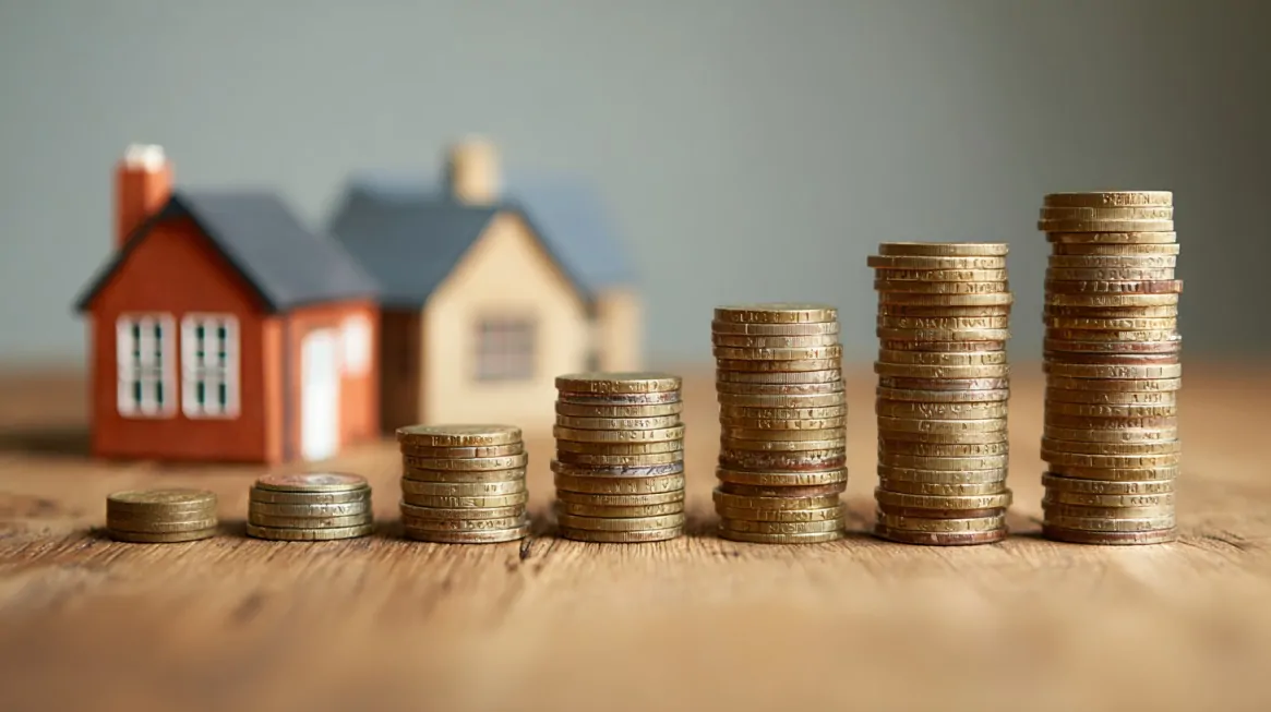 Stacks of coins increasing in size in front of small model houses