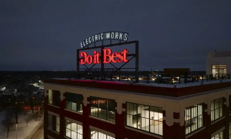 Red neon sign "Do it Best" atop a large building with "Electric Works" illuminated above it at night, set against a dark sky
