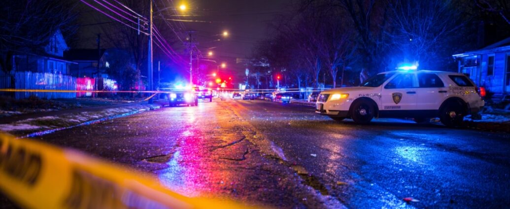Police cars with flashing lights blocking a street at night with crime scene tape in the foreground