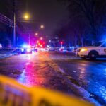 Police cars with flashing lights blocking a street at night with crime scene tape in the foreground