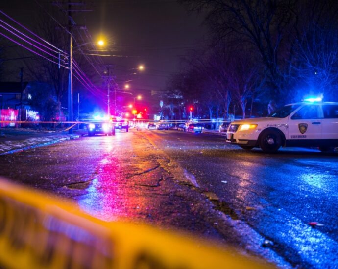 Police cars with flashing lights blocking a street at night with crime scene tape in the foreground