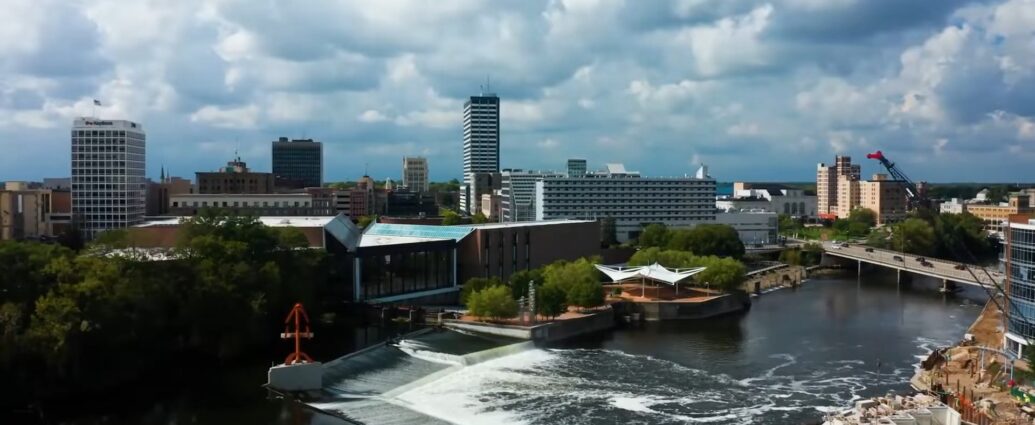 Cityscape of South Bend Indiana showing buildings, river, dam, and bridges under a partly cloudy sky