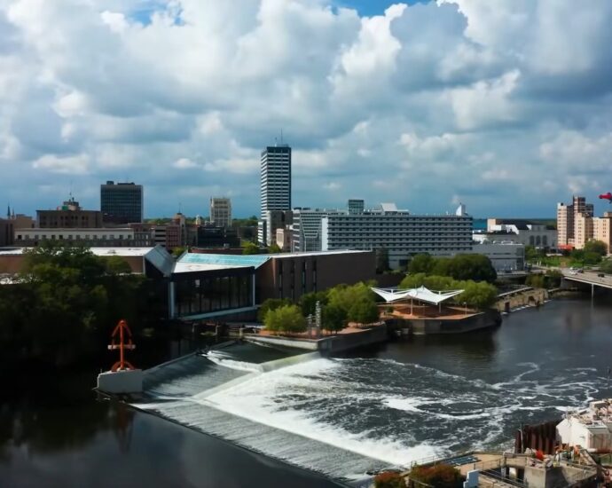 Cityscape of South Bend Indiana showing buildings, river, dam, and bridges under a partly cloudy sky