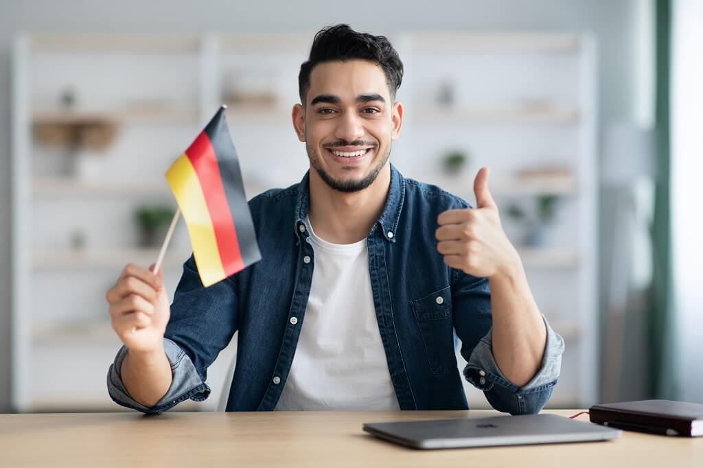Man holding German flag and smiling while sitting at desk with laptop
