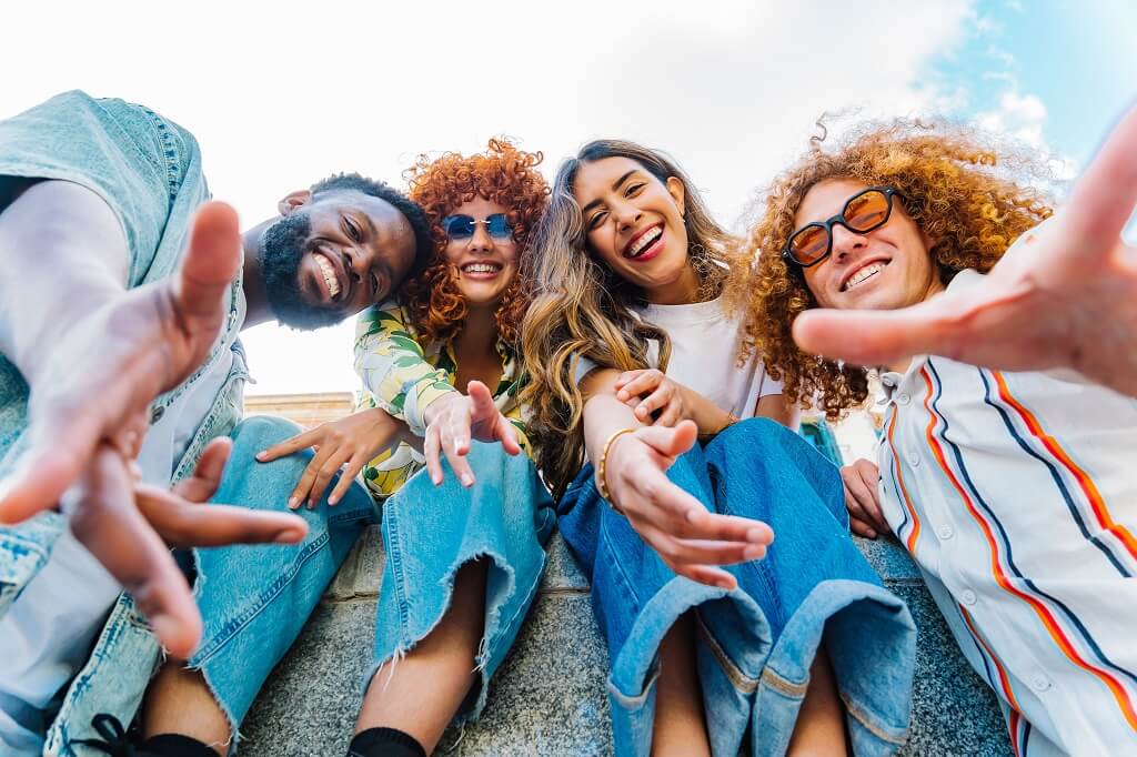 Diverse group of young people smiling and reaching toward camera outdoors