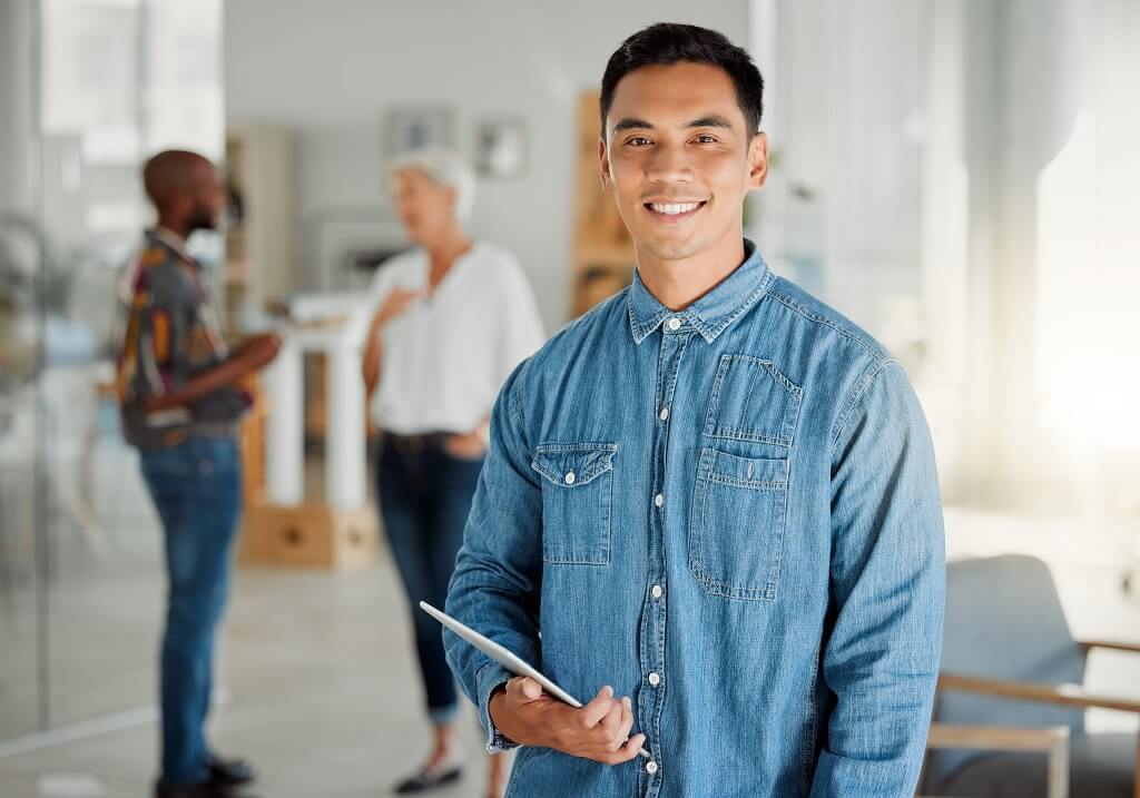 Man holding tablet in office with diverse coworkers talking in background