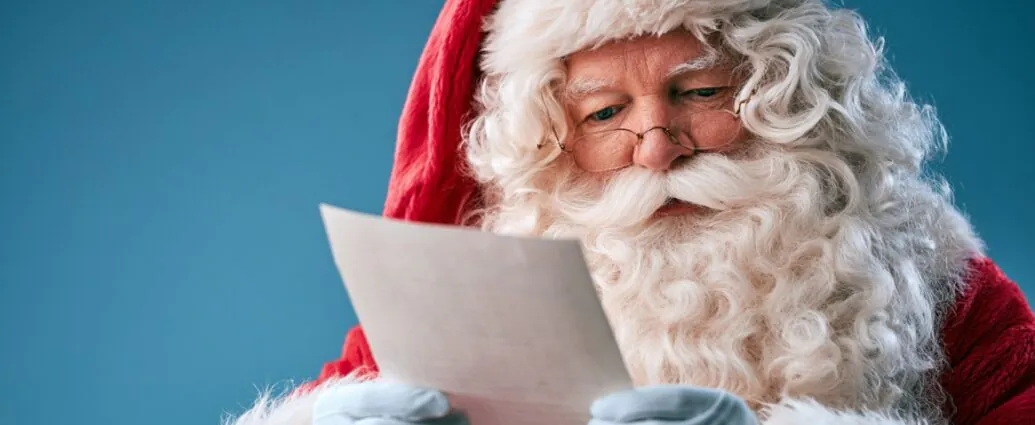 Santa Claus reading a handwritten letter while wearing his classic red suit and white gloves