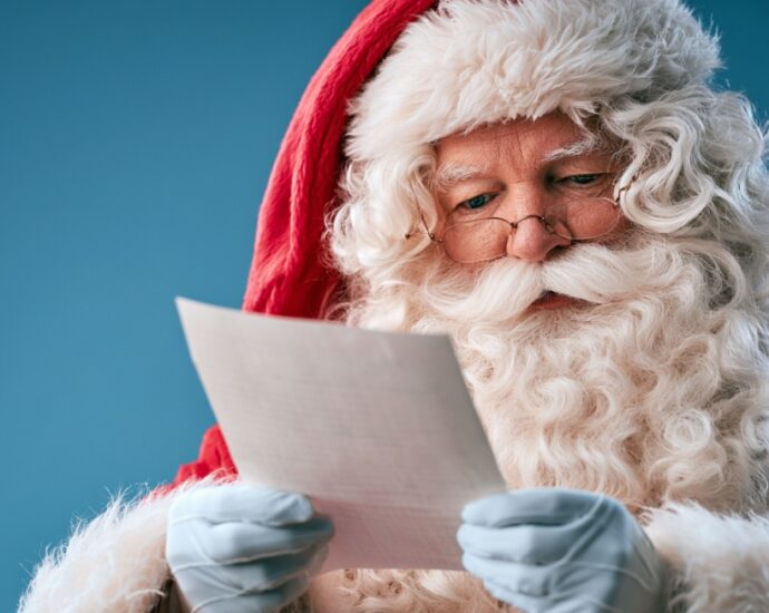 Santa Claus reading a handwritten letter while wearing his classic red suit and white gloves