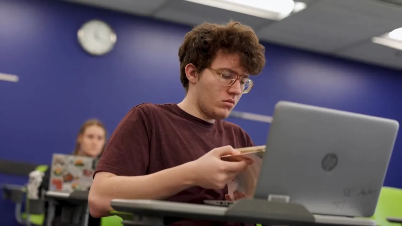 A college student reads beside a laptop in a classroom