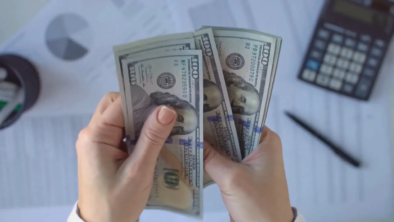 Hands count US dollar bills beside a calculator and financial documents