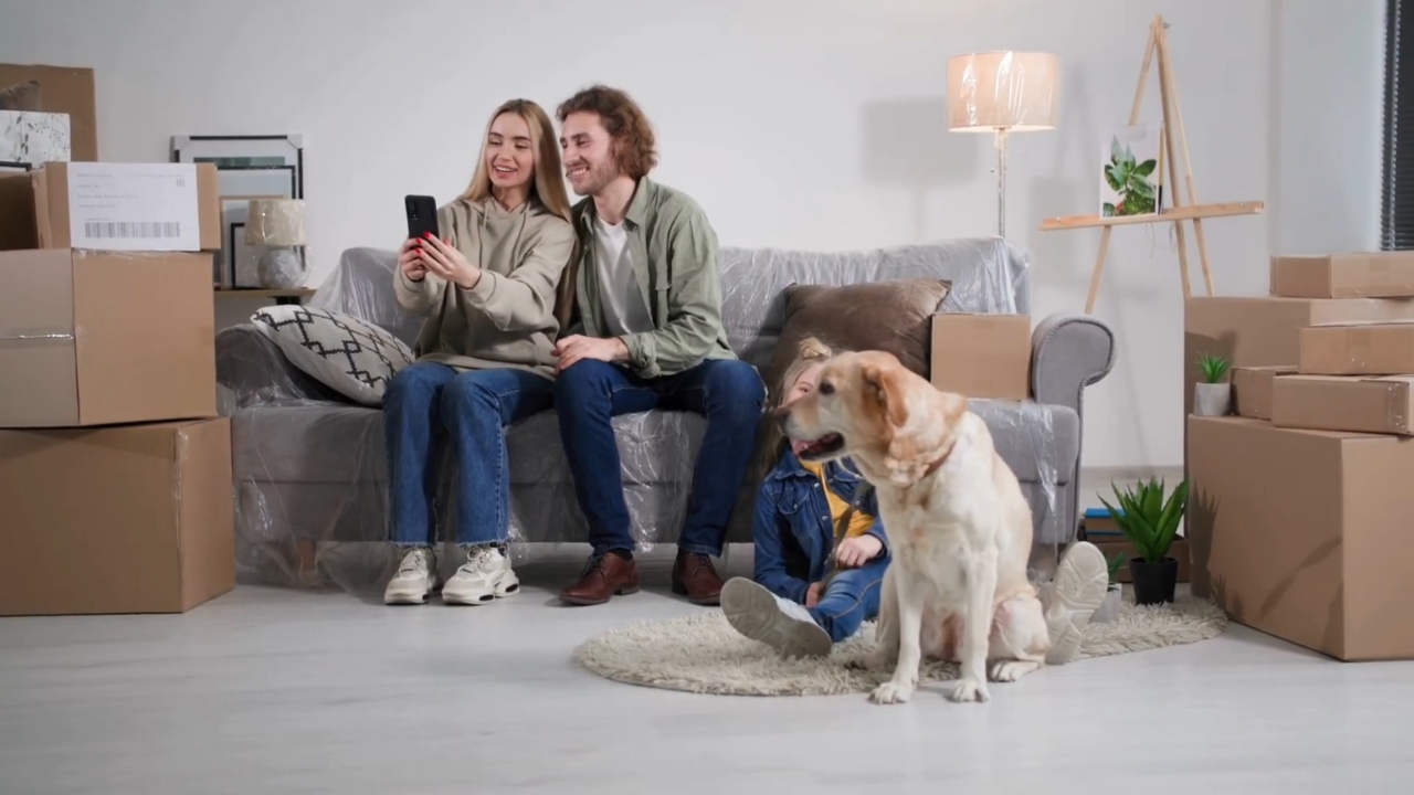 A family sits among packed boxes with their dog in a new home