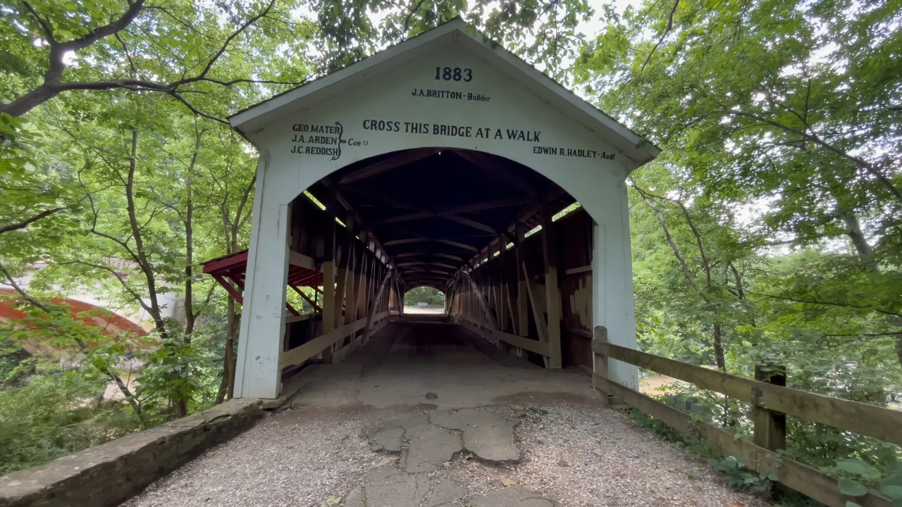 A covered bridge entrance sits under trees along a Parke County route