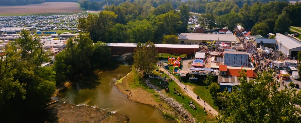 Aerial view of the Covered Bridge Festival with vendor booths, crowds, a covered bridge, and packed fields of cars