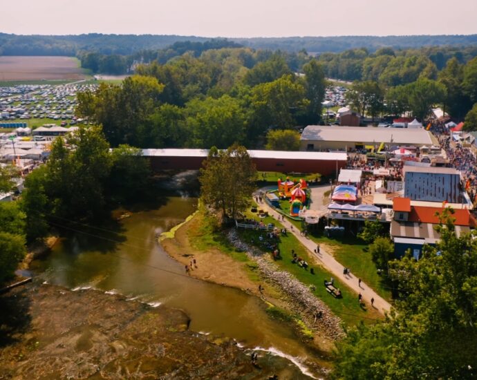 Aerial view of the Covered Bridge Festival with vendor booths, crowds, a covered bridge, and packed fields of cars