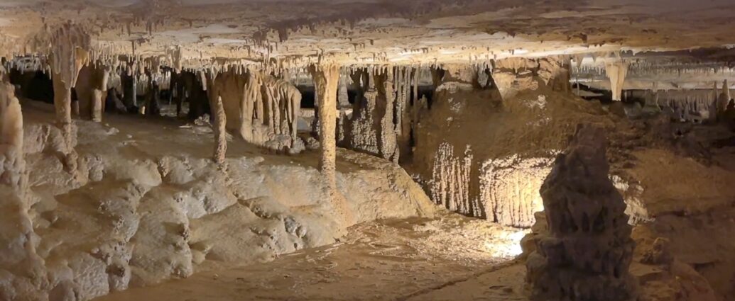 Lit cave chamber with stalactites, stalagmites, and mineral columns