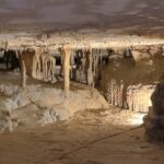 Lit cave chamber with stalactites, stalagmites, and mineral columns