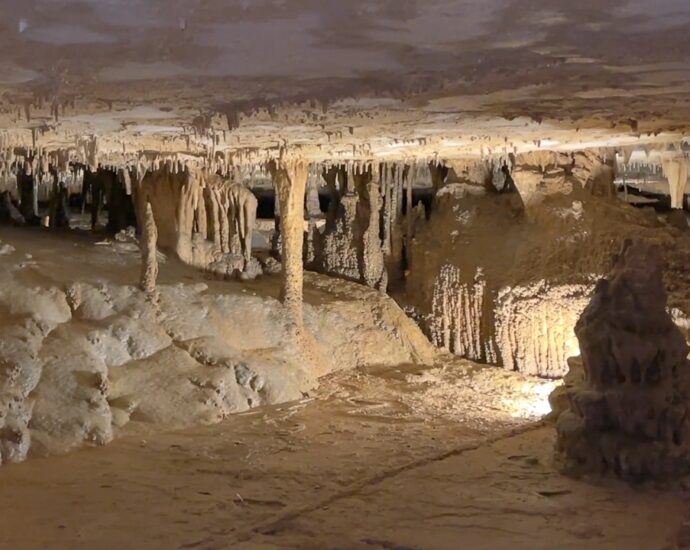 Lit cave chamber with stalactites, stalagmites, and mineral columns