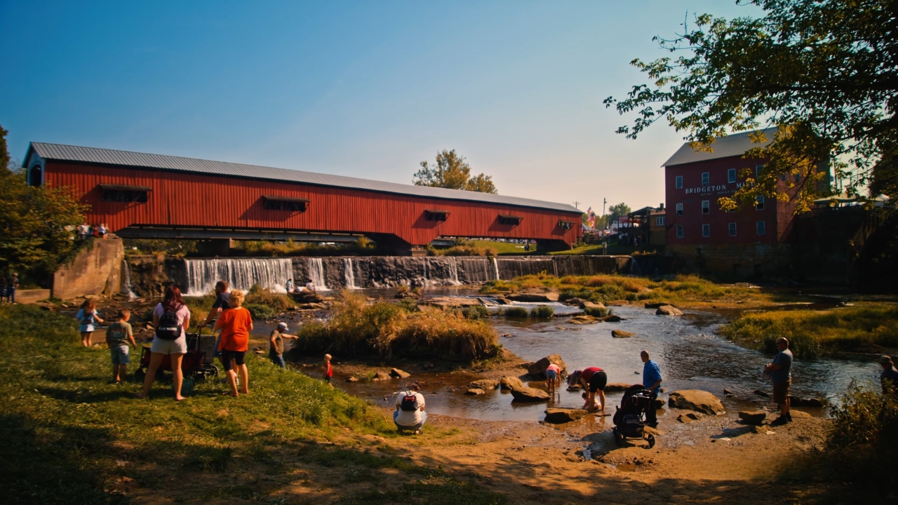 Visitors gather beside Bridgeton Covered Bridge and Mill along the creek in Parke County