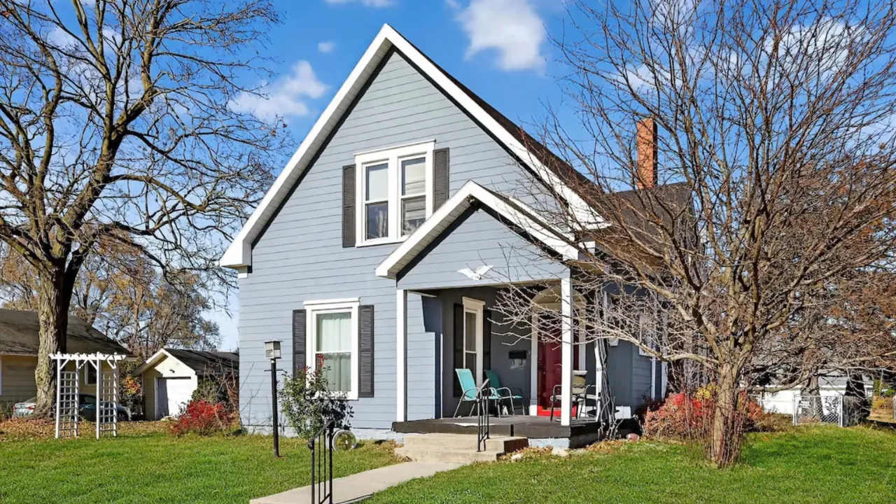 A gray two-story house with a red front door and a small lawn