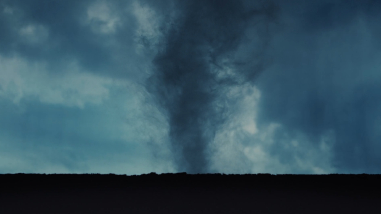 Dark tornado funnel beneath storm clouds over a flat landscape.