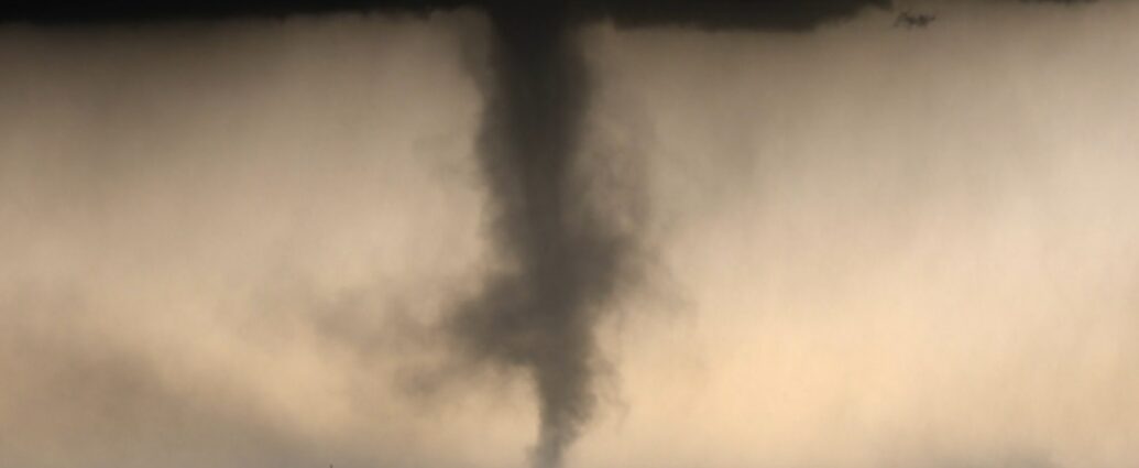 A large tornado funnel beneath dark storm clouds over a flat landscape.