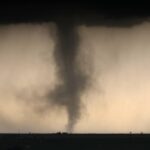A large tornado funnel beneath dark storm clouds over a flat landscape.