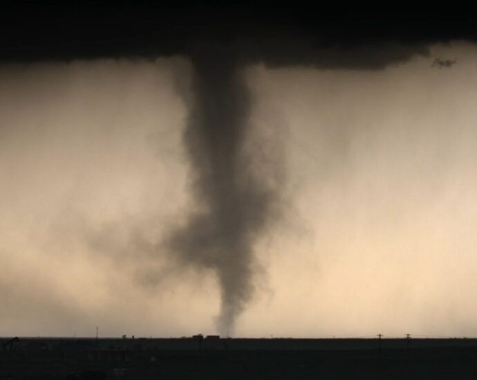 A large tornado funnel beneath dark storm clouds over a flat landscape.